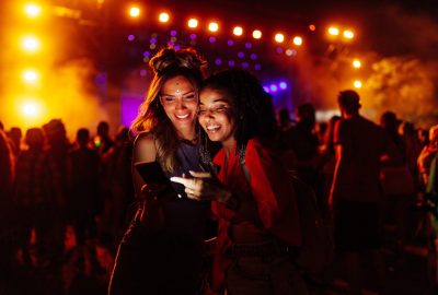 Two,Biracial,Women,In,A,Crowd,At,A,Concert,Using